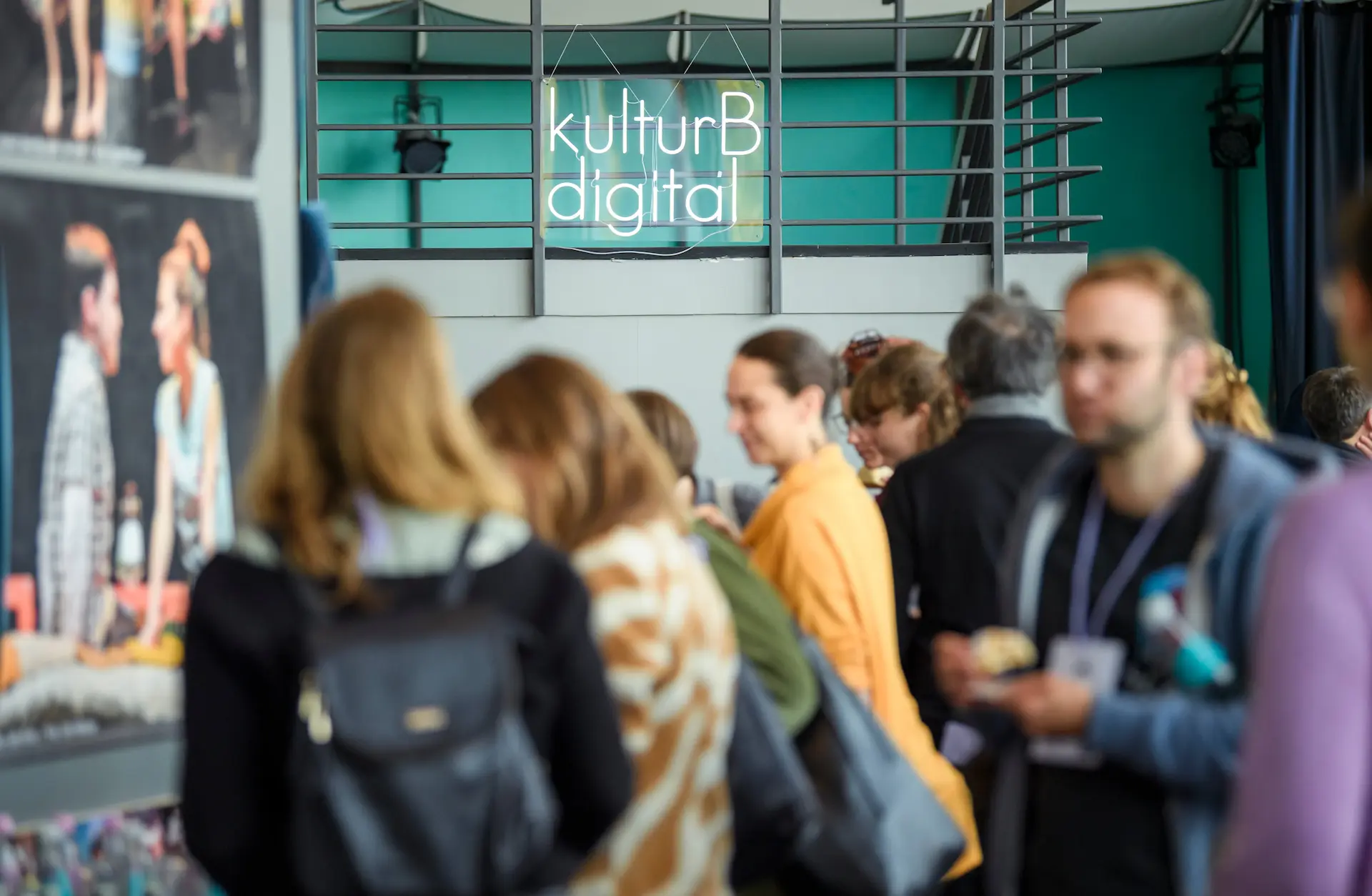 Eine unscharfe Menschenmenge während der Konferenz, ein Neonschriftzug von kulturBdigital im Hintergrund.