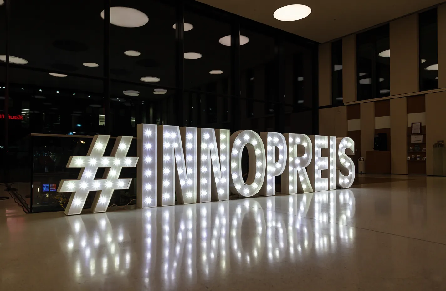 Beleuchtete 3D-Schriftzug mit dem Hashtag Innopreis in einem abgedunkelten Foyer.